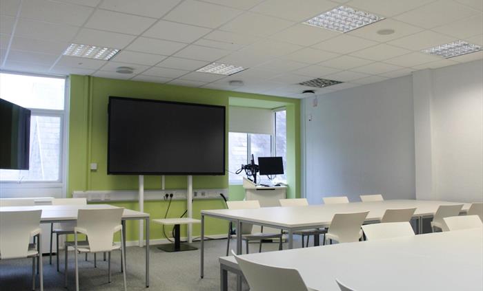 Classroom with tables, chairs and tv screen.